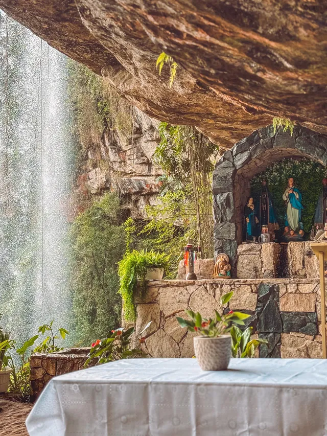 Cachoeira alta caindo ao lado da gruta com capela no Poço Certo