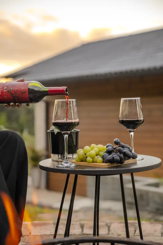 Vinho sendo servido numa mesinha no deck, com uvas, no fim da tarde