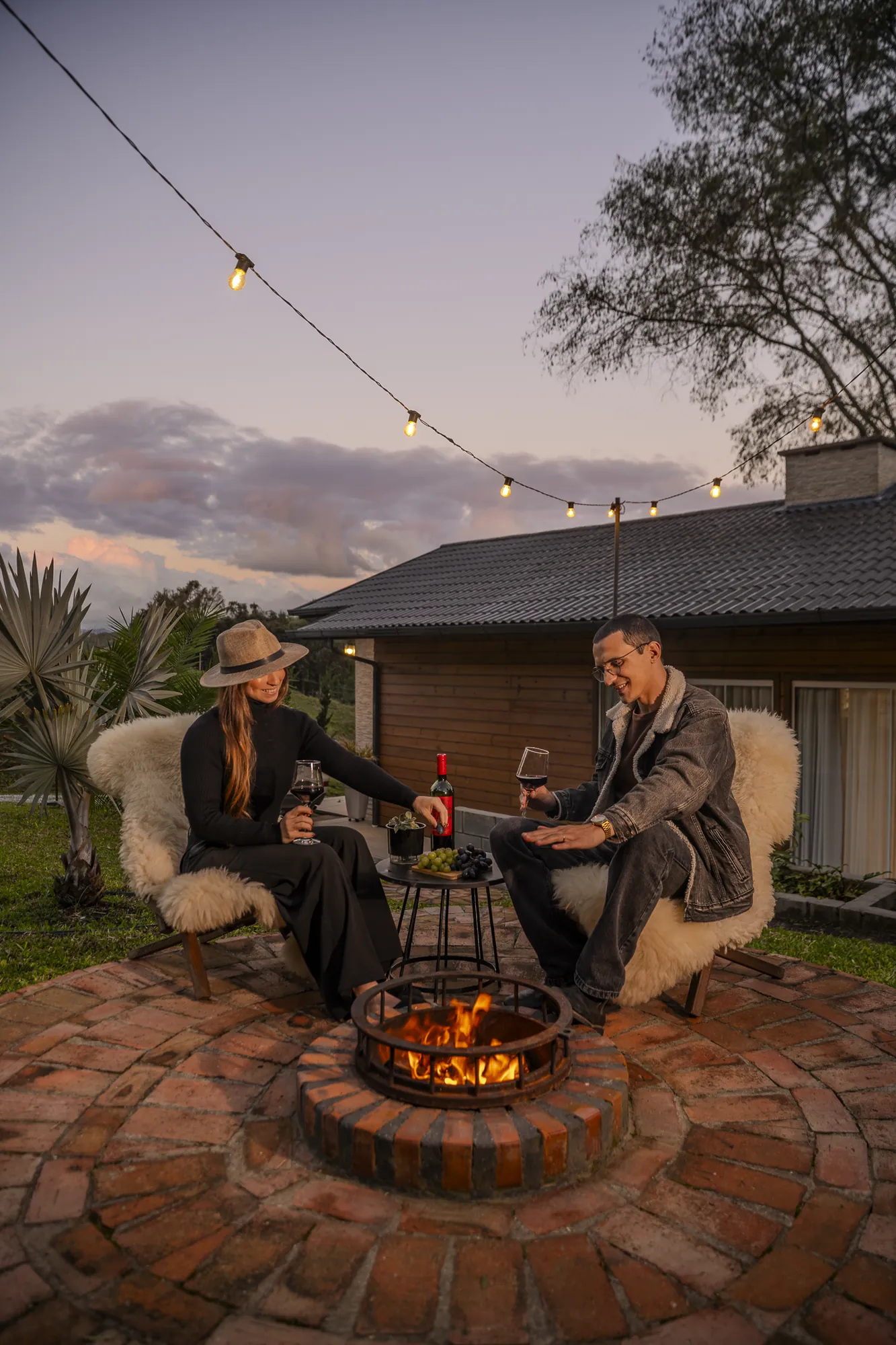 Casal no fogo de chão da Cabana ao entardecer, com as luzinhas acesas