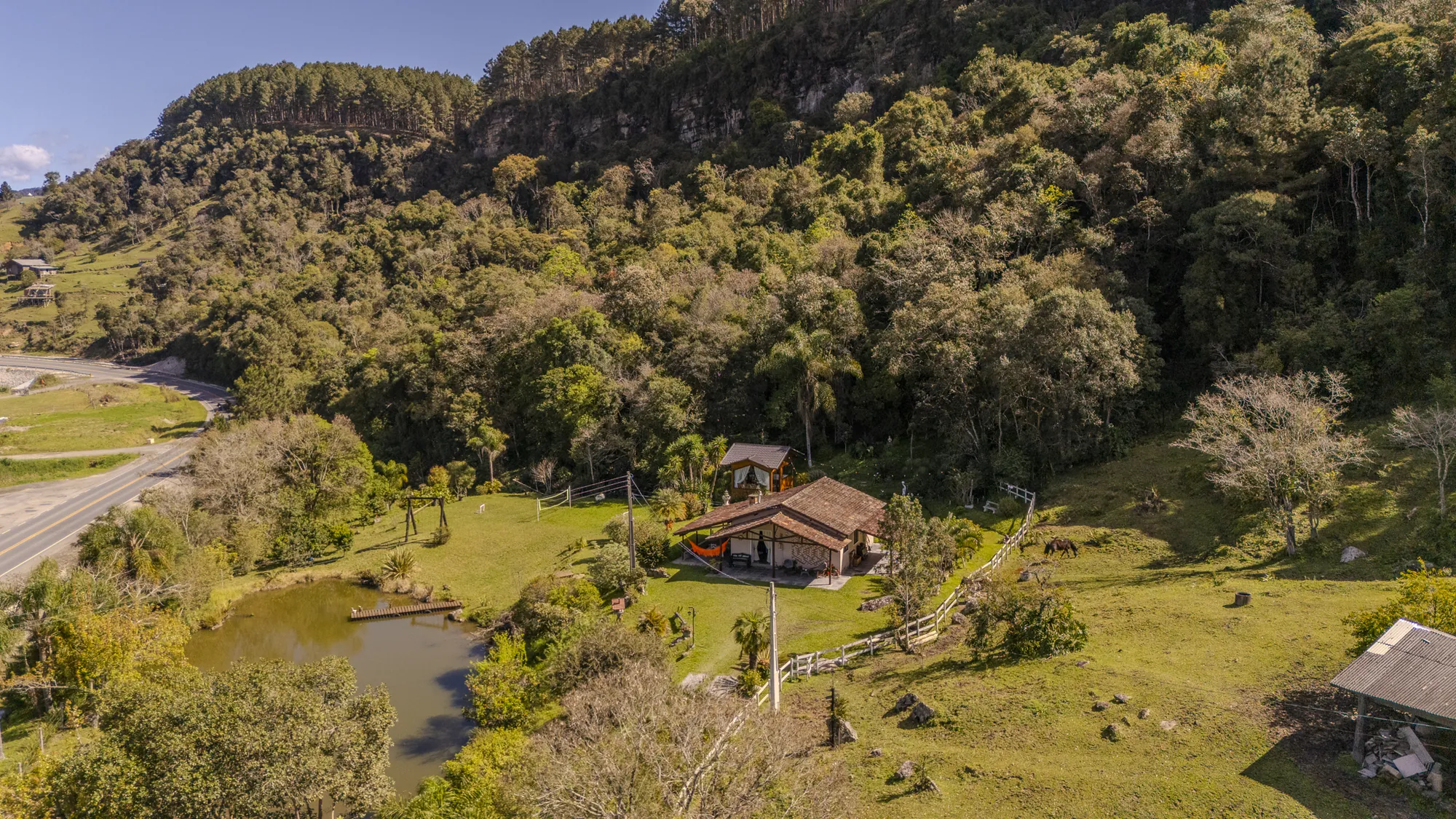 O vale da pousada visto do alto, com a mata, o lago e as duas hospedagens no meio dos gramados