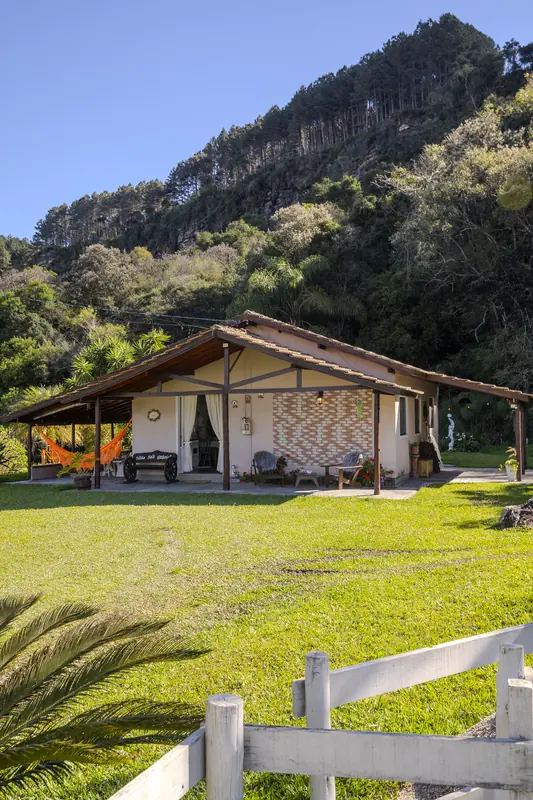 A Casa da Belina no gramado, com a cerca branca e o paredão de mata atrás