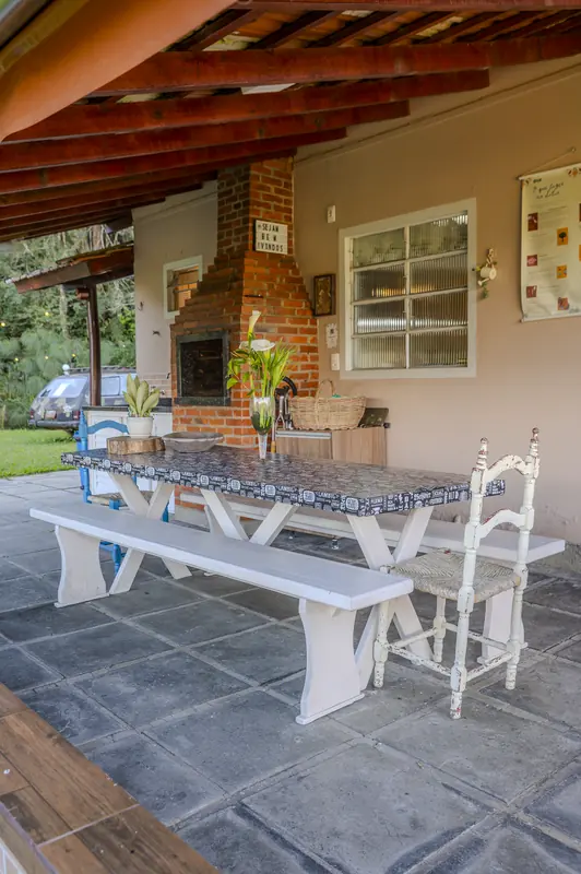Varanda com churrasqueira de tijolo e mesa comprida com bancos